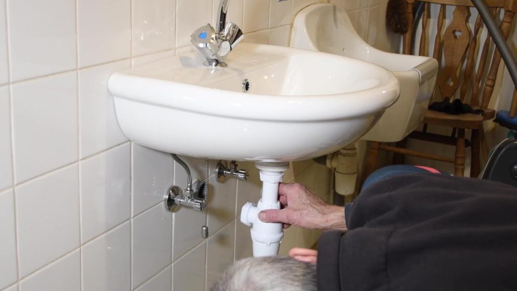 Plombier démontant et remplaçant le siphon sous un évier à Douala, joints et raccords visibles